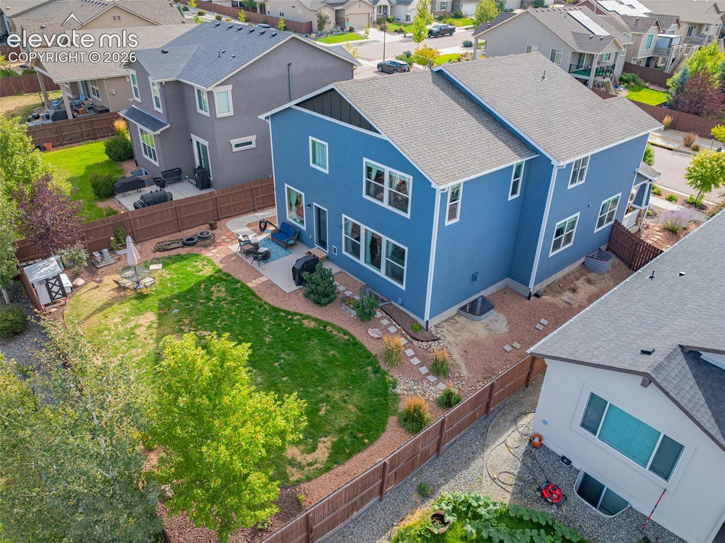 Aerial view of a blue two-story home and its fenced backyard with patio seating and lawn.