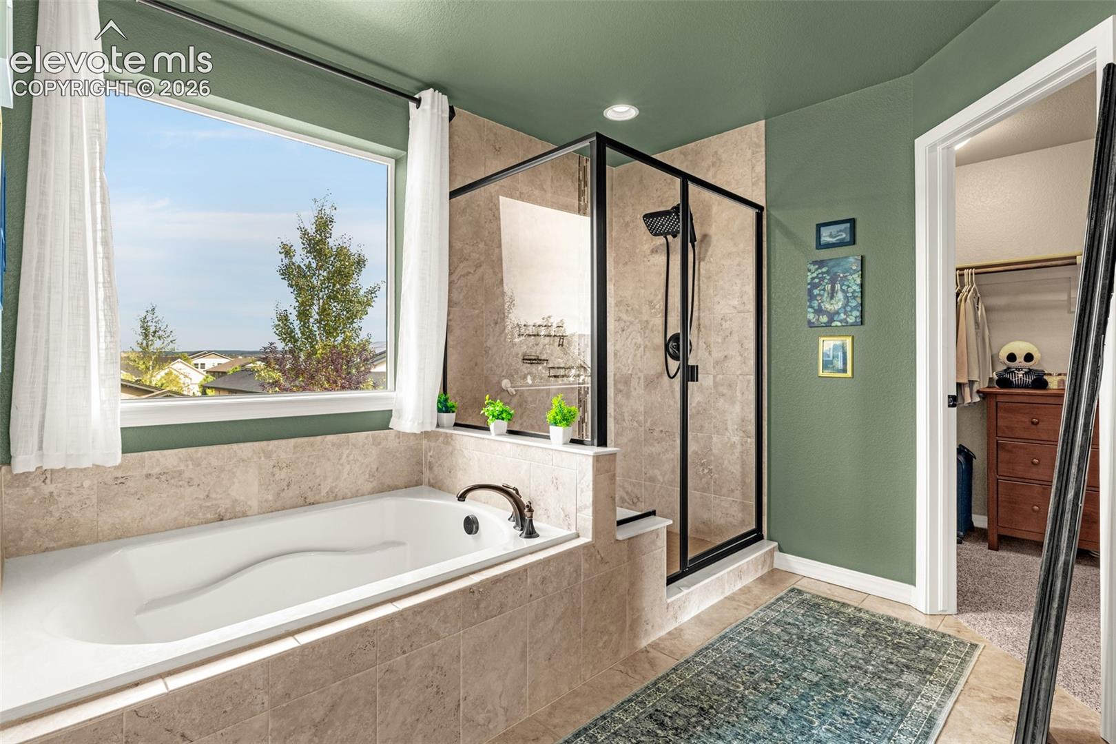Bathroom with a tiled soaking tub beneath a large window and a black-framed glass shower.