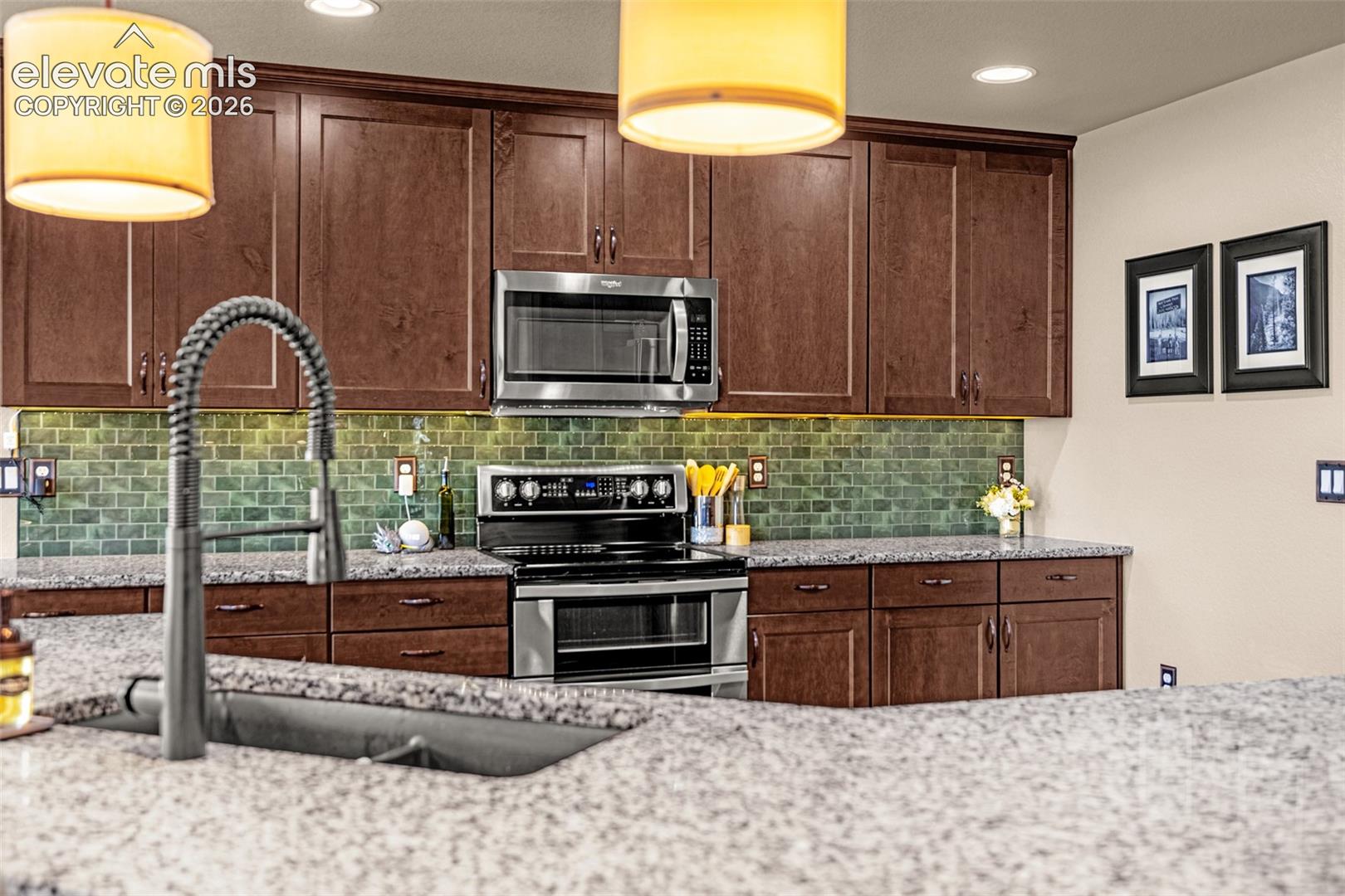 Kitchen with dark wood cabinets, green tile backsplash, granite counters, stainless steel appliances, and a large island sink.