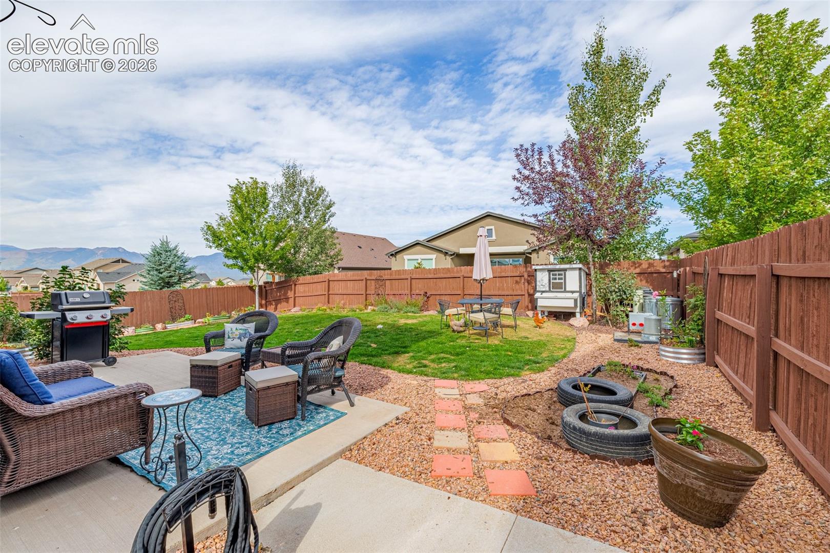 Fenced backyard with patio seating, gravel garden paths, and distant mountain views.