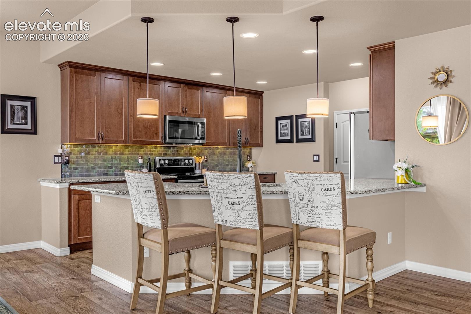 Kitchen with dark wood cabinetry, green tile backsplash, and a breakfast bar with three stools.