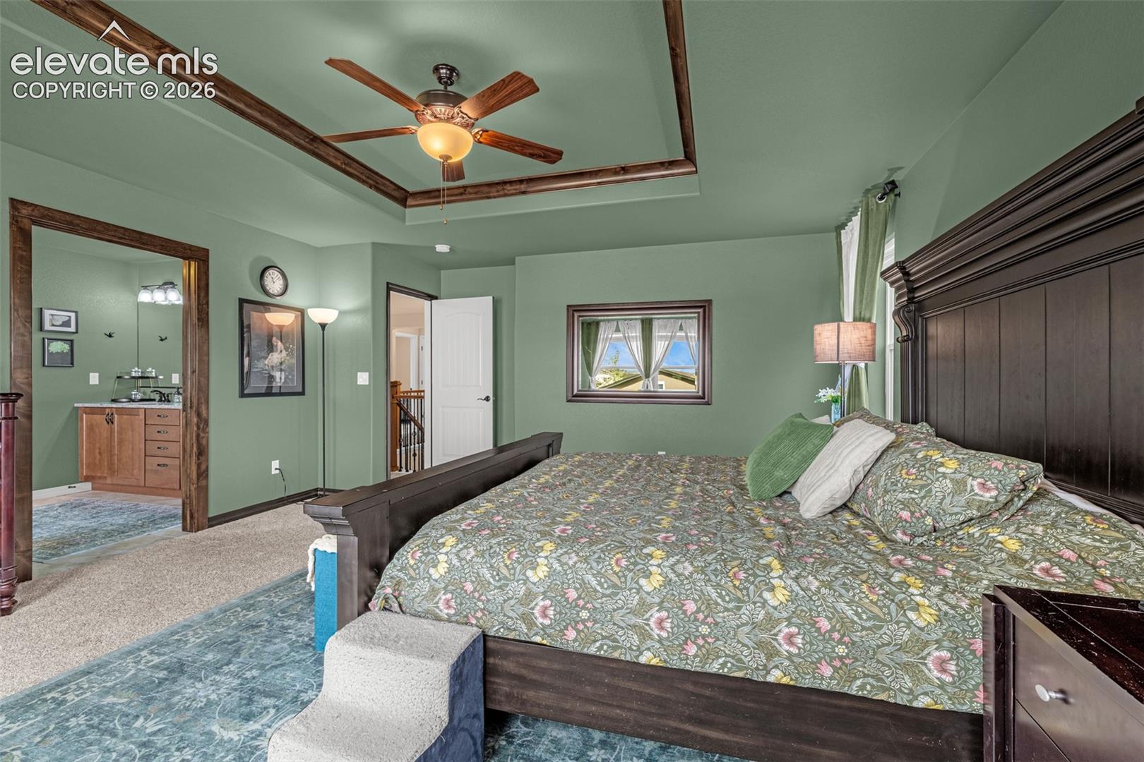 Furnished bedroom with sage green walls, floral bedding, dark wood furniture, and a tray ceiling.