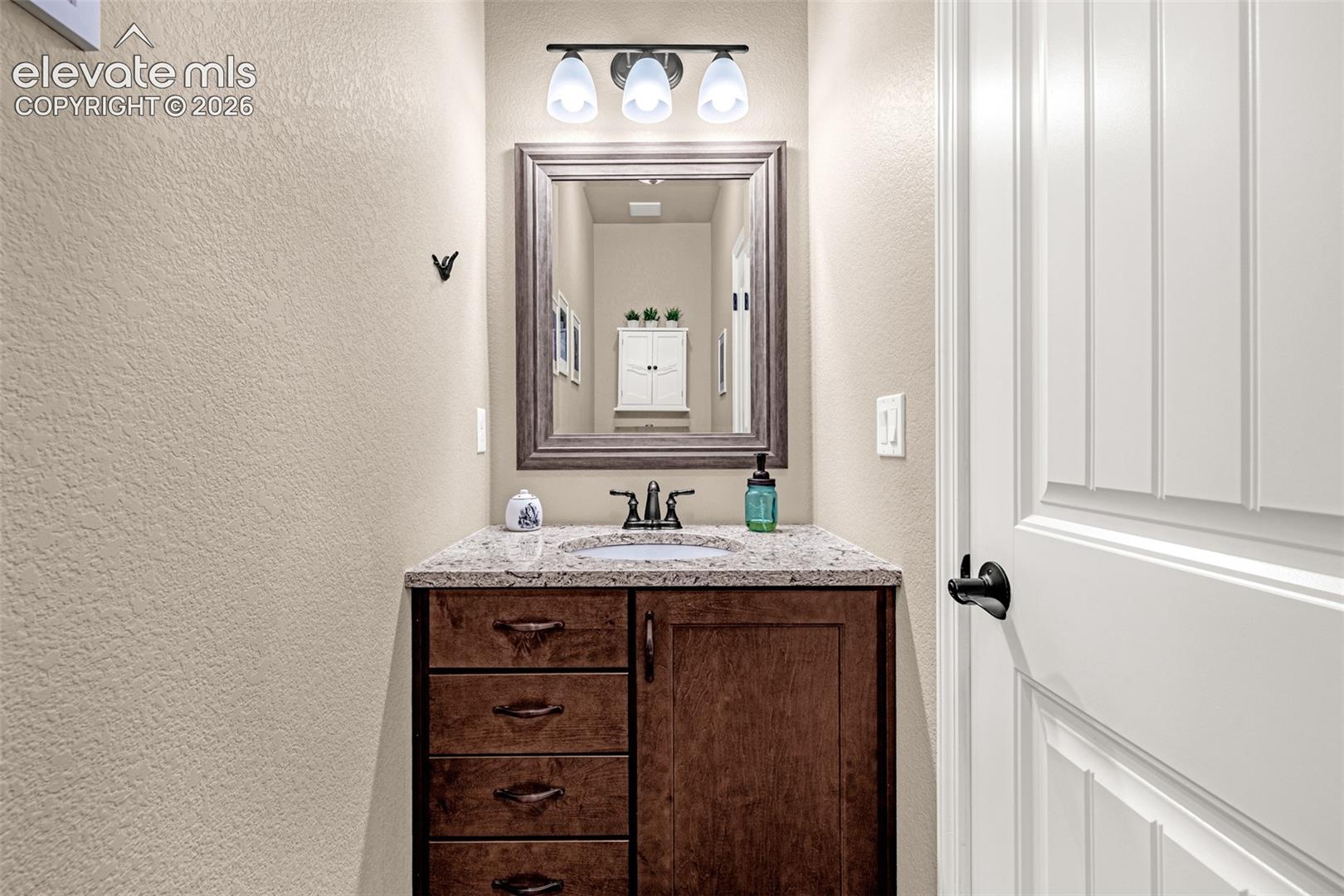 Bathroom vanity with dark wood cabinetry, granite countertop, black faucet, and framed mirror.