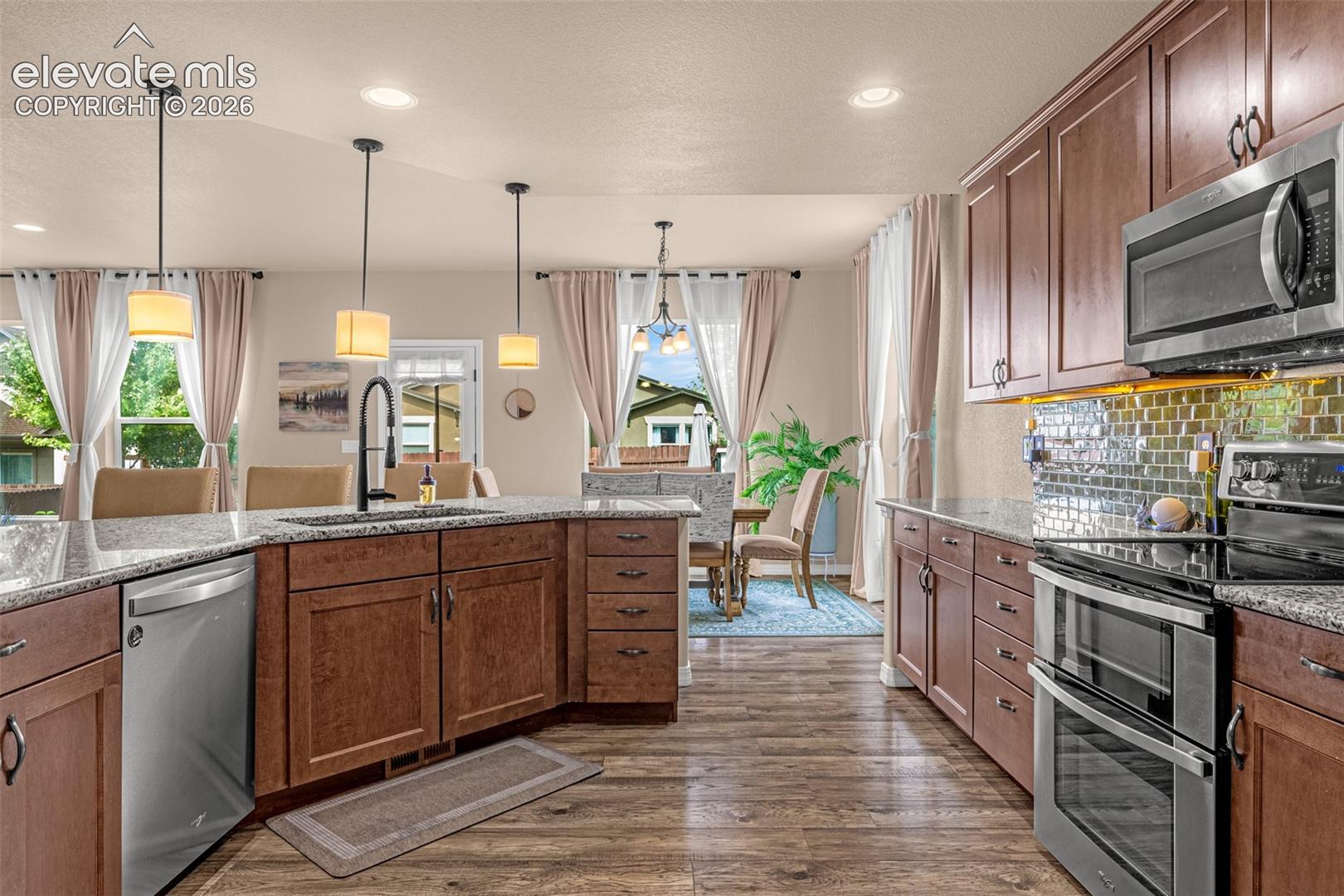 Kitchen with wood cabinets, granite counters, stainless steel appliances, and an island sink.