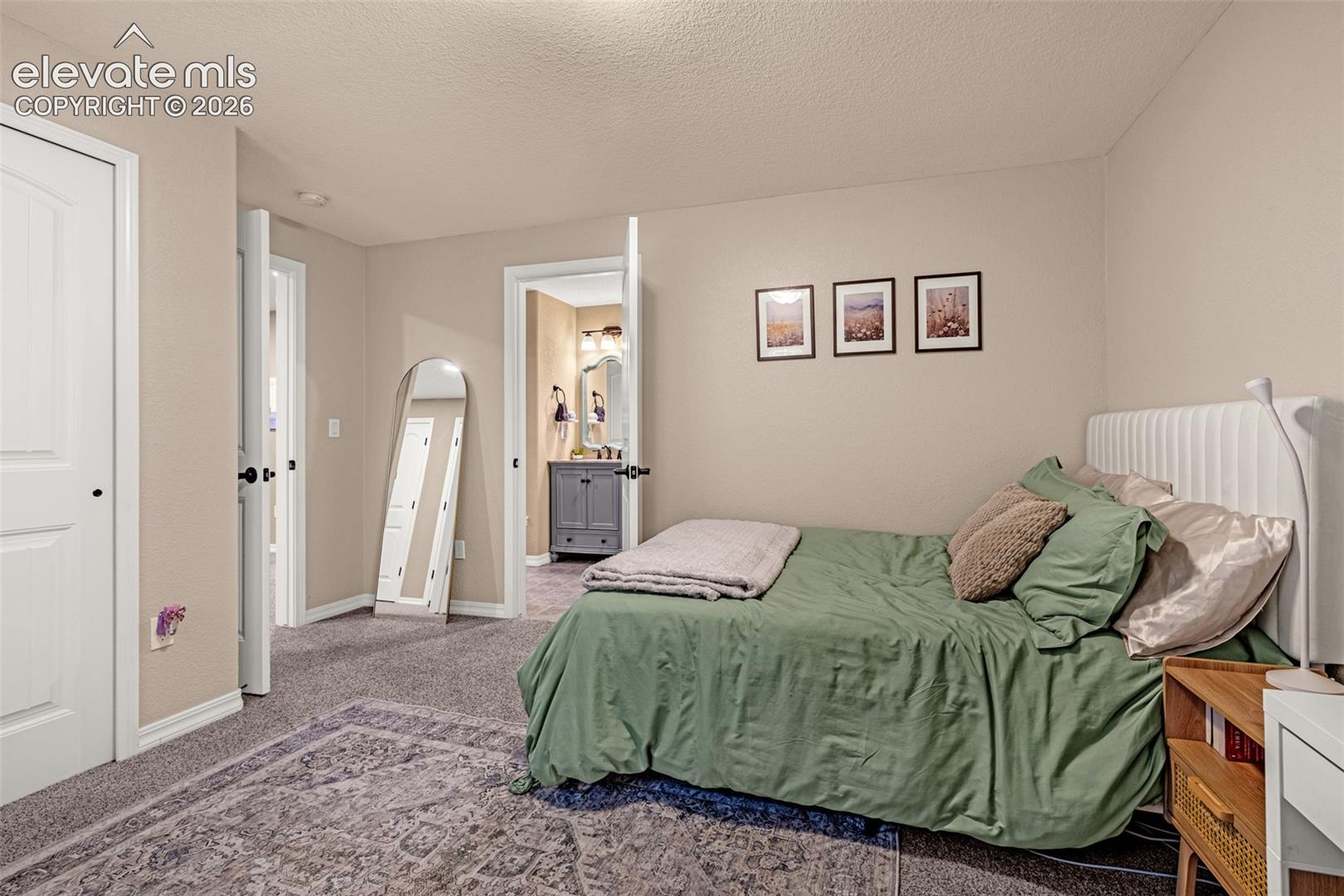 Bedroom with green bedding, white upholstered headboard, and open doorway to a bathroom.