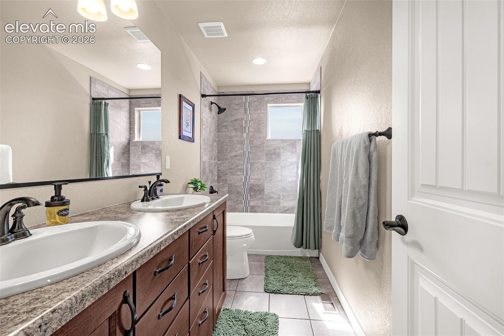 Bathroom with a double-sink vanity and tiled tub and shower behind a green curtain.