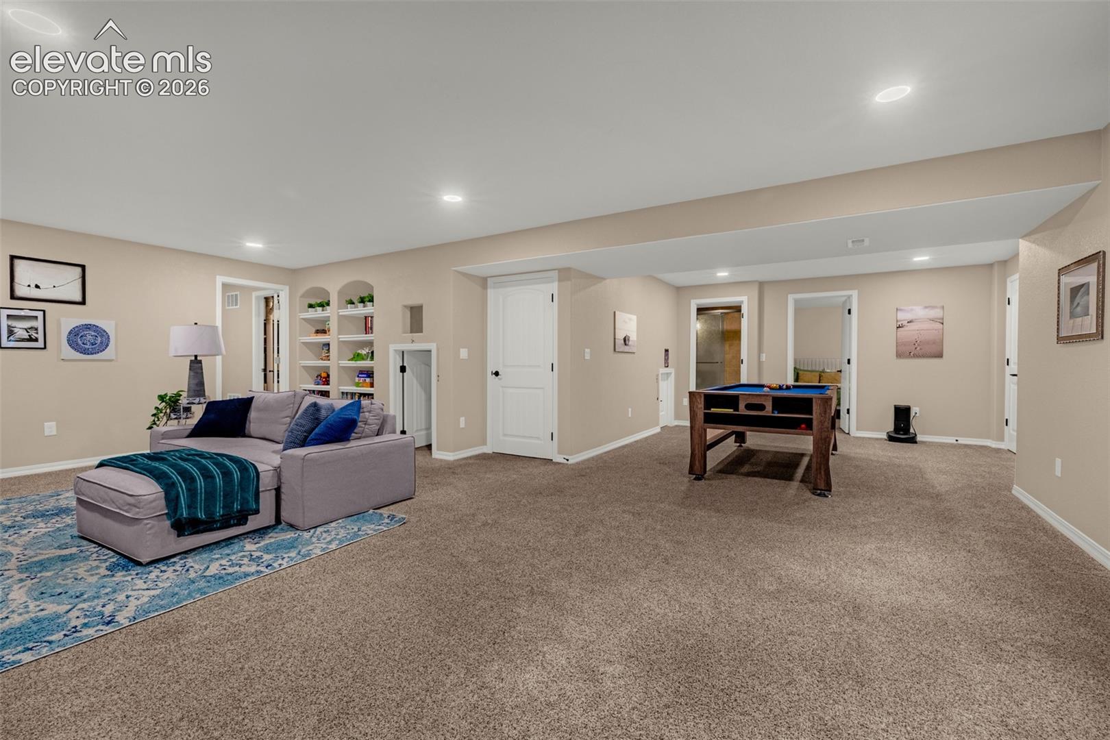 Basement recreation room with a gray sectional, blue rug, built-in shelves, and a pool table.
