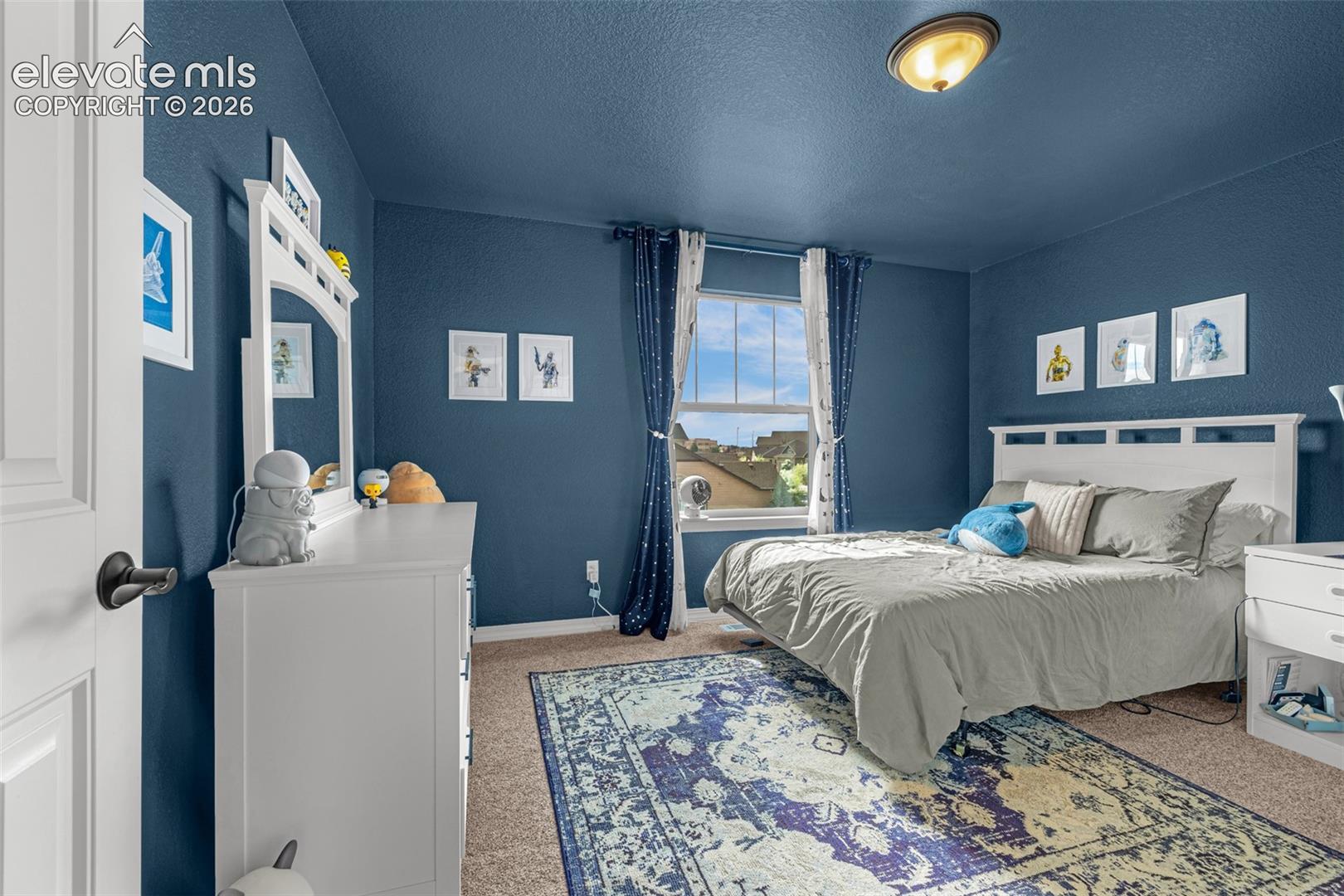 Bedroom with deep blue walls, white furniture, neutral bedding, and space-themed decorations.