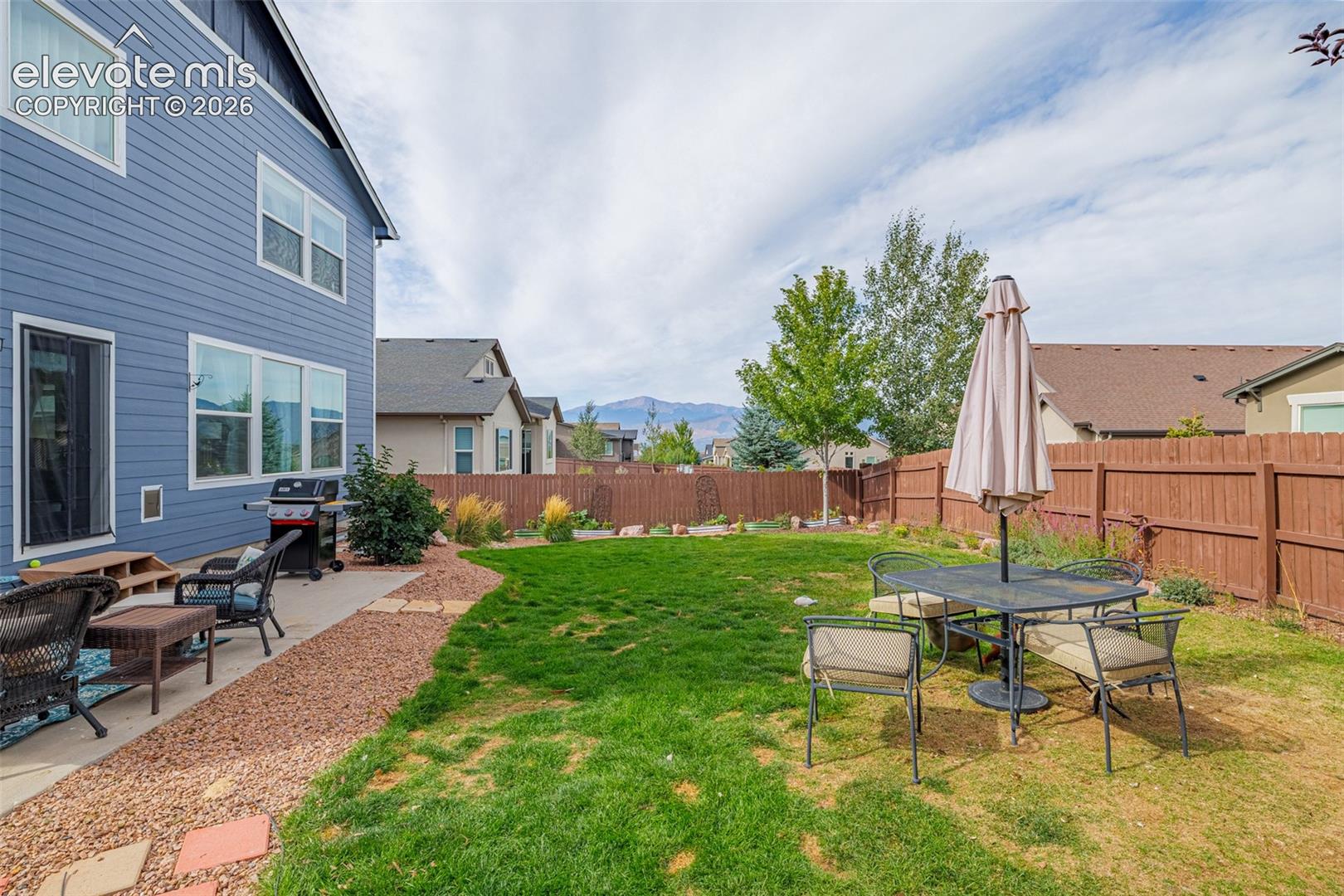 Fenced backyard with lawn, patio seating, grill, and distant mountain views.