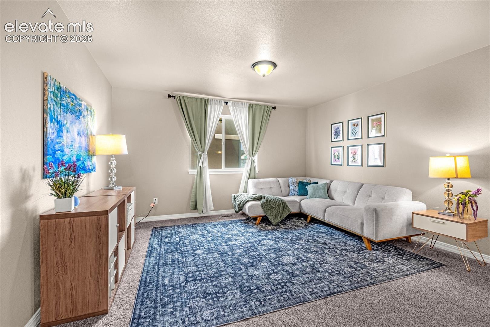 Staged living room with a gray sectional, blue patterned rug, and floral artwork.