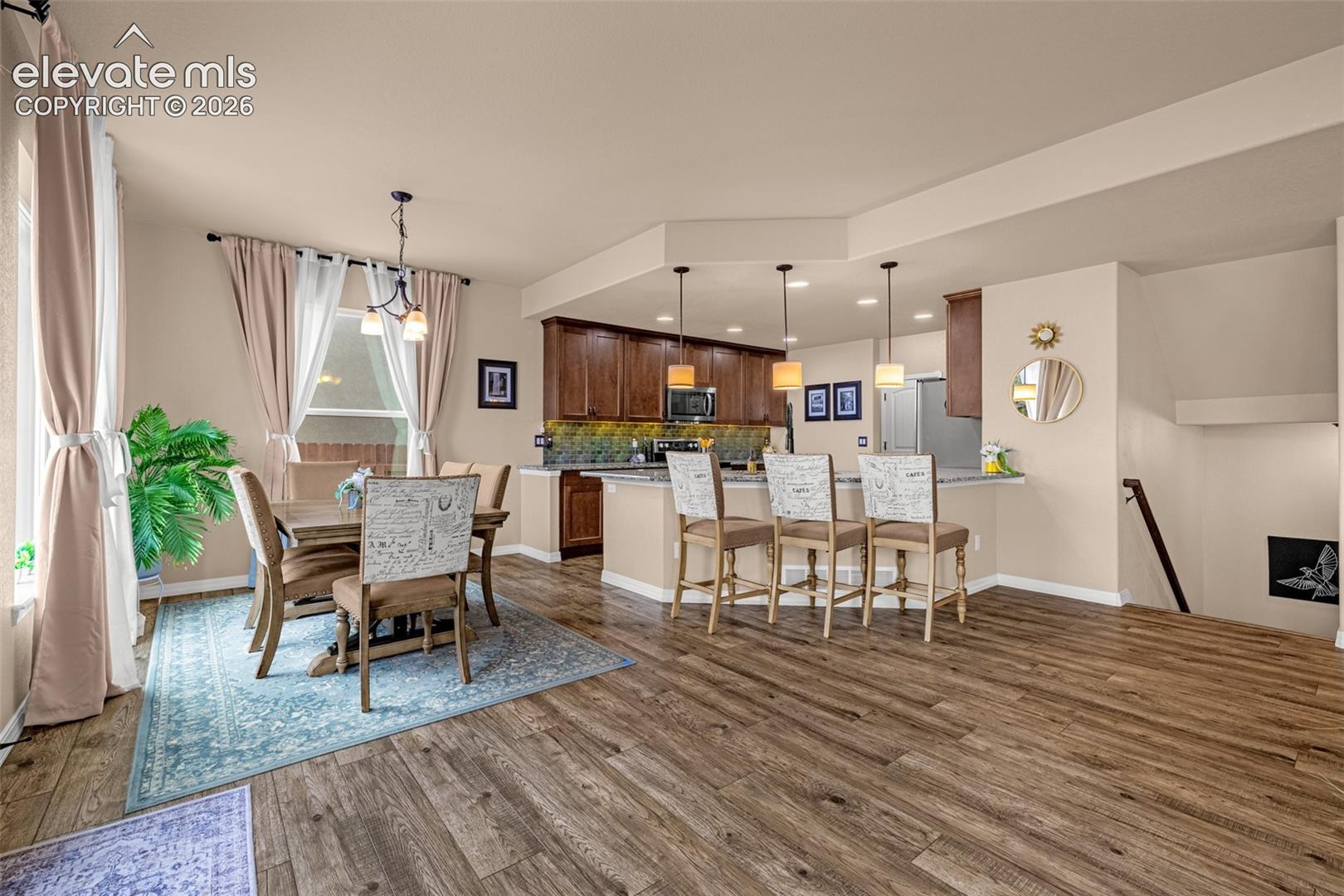 Open-plan kitchen and dining area with dark cabinets, breakfast bar, and wood-look floors.