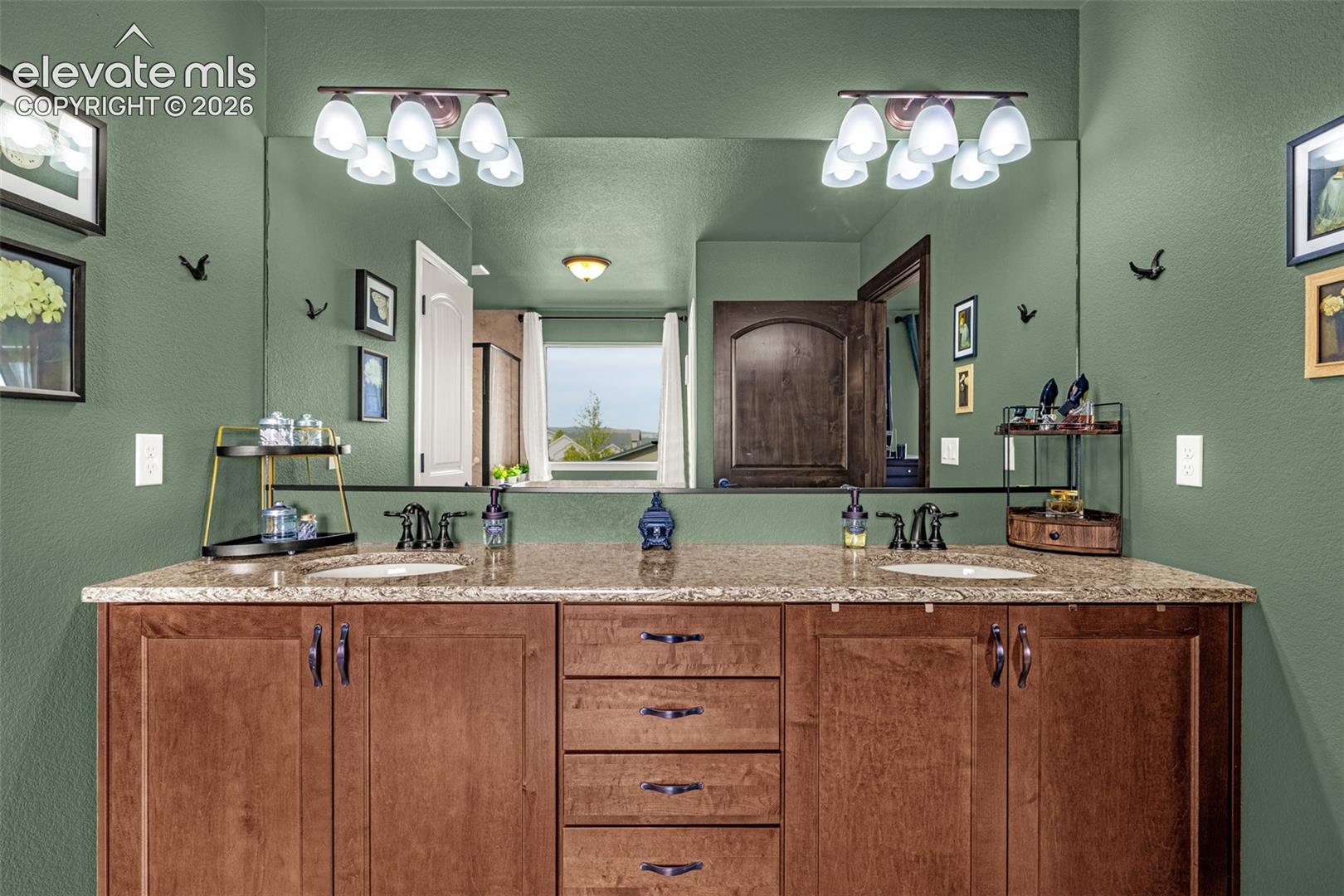 Bathroom vanity with two sinks, warm wood cabinetry, stone countertop, and a large mirror.