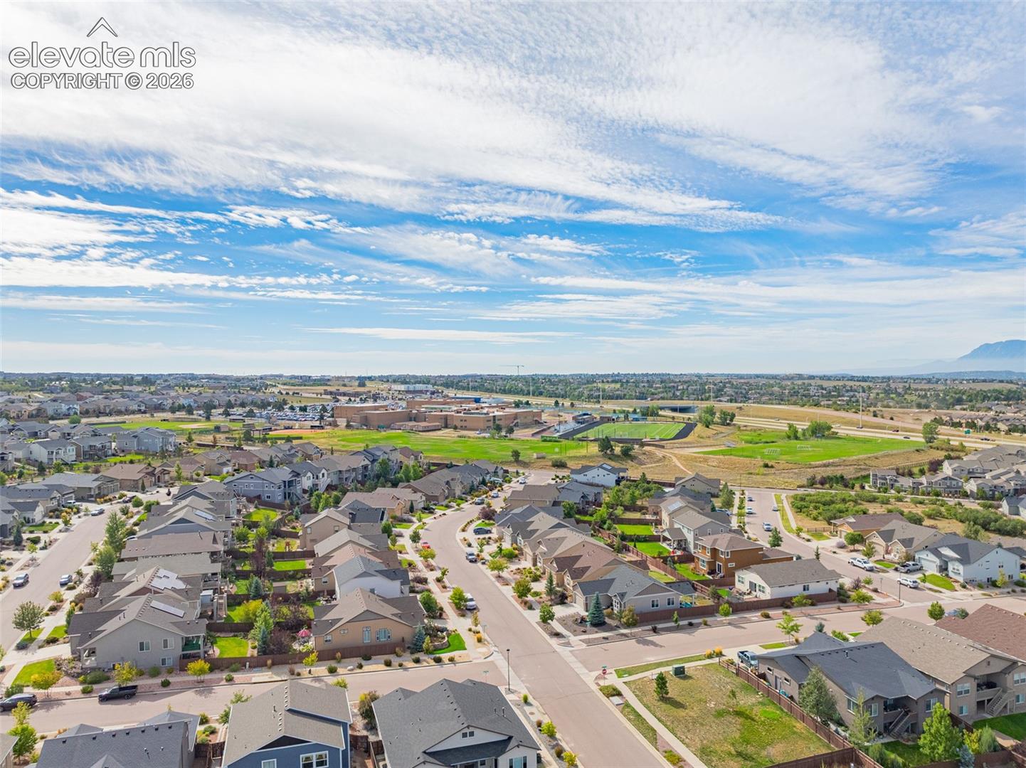 Aerial view of a residential neighborhood with school fields and distant mountains.
