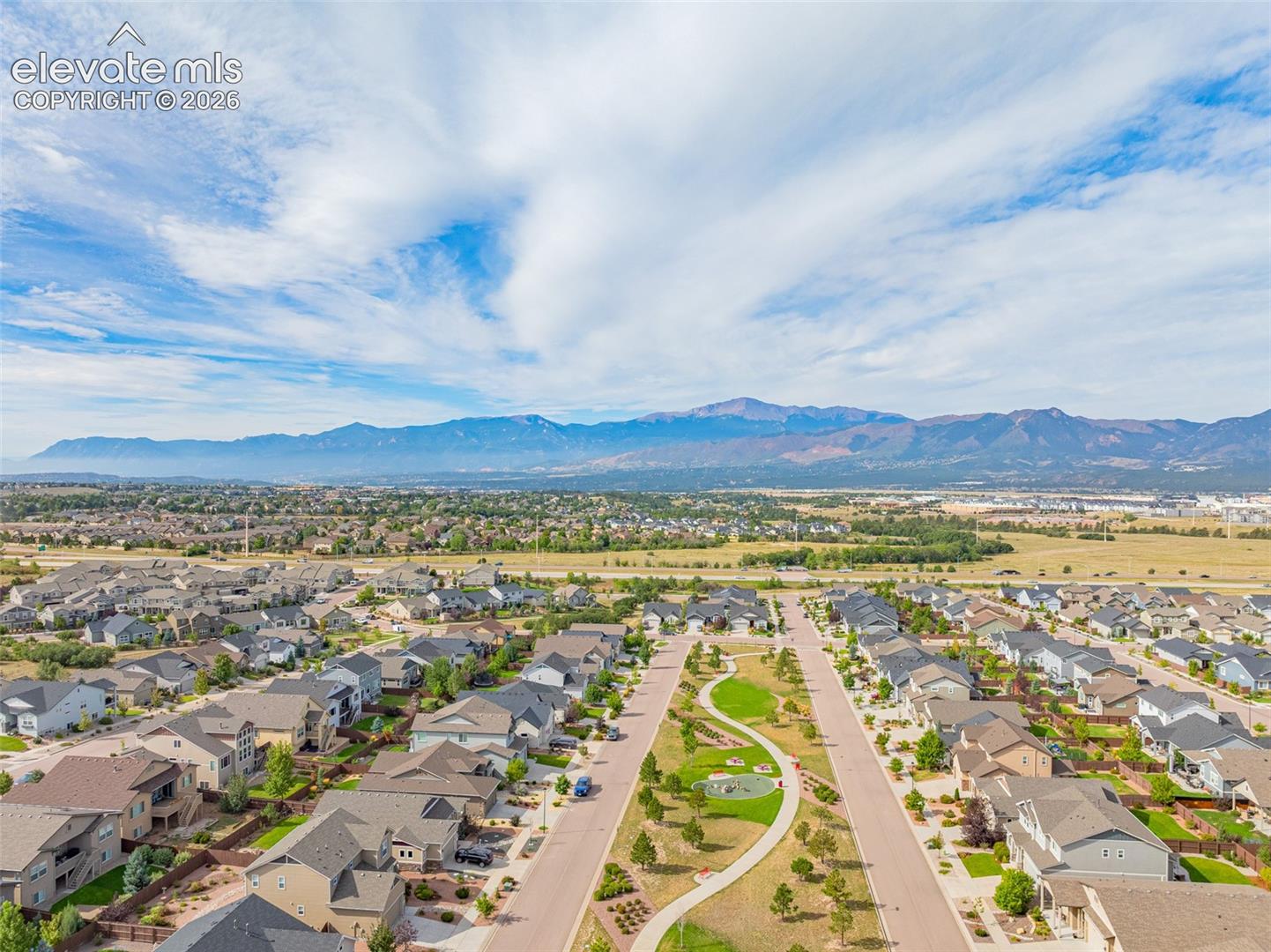 Aerial view of a Colorado Springs neighborhood with a central park and mountains on the horizon.