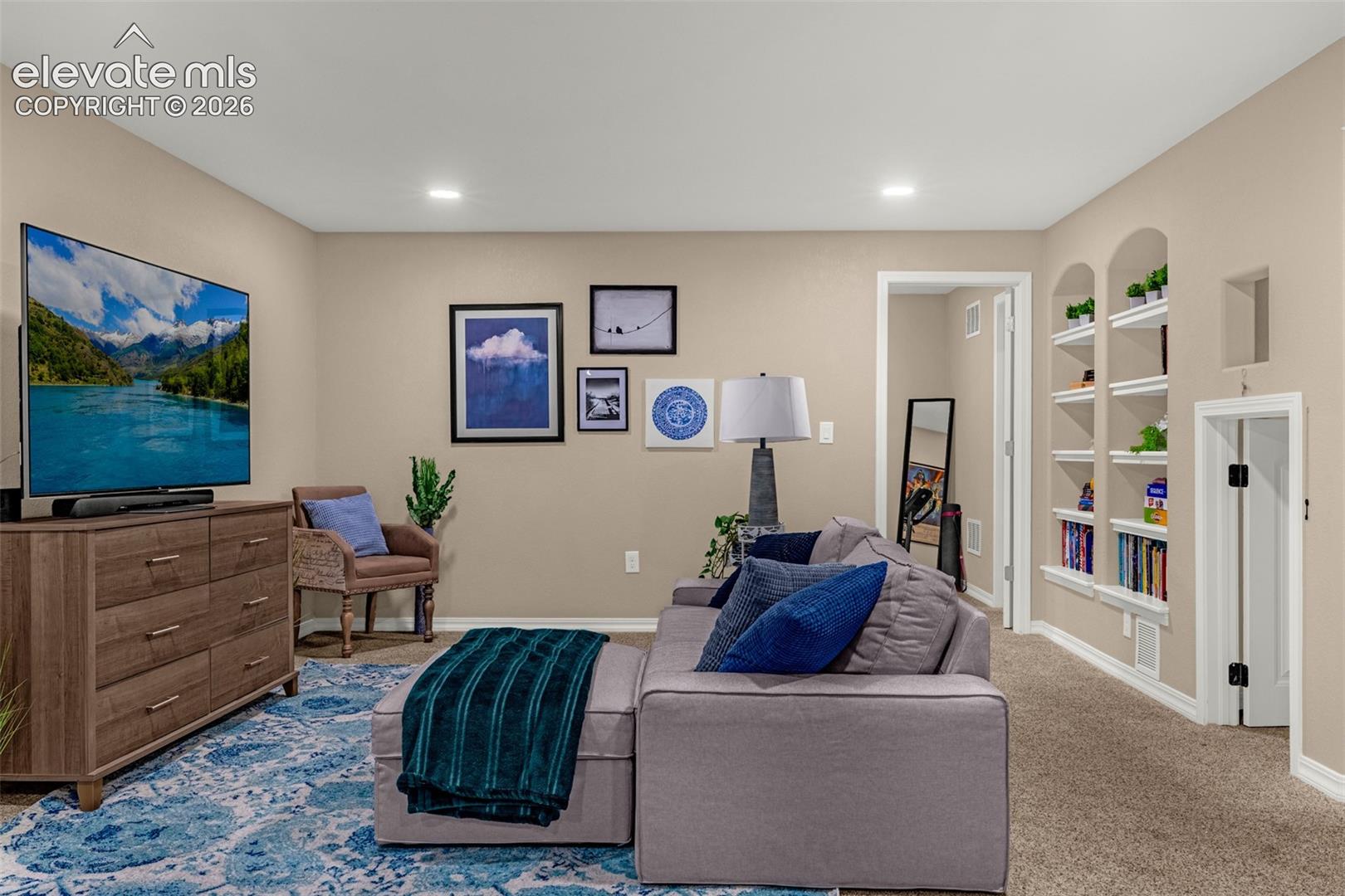 Furnished living room with a gray sectional, blue accents, and built-in display shelves.