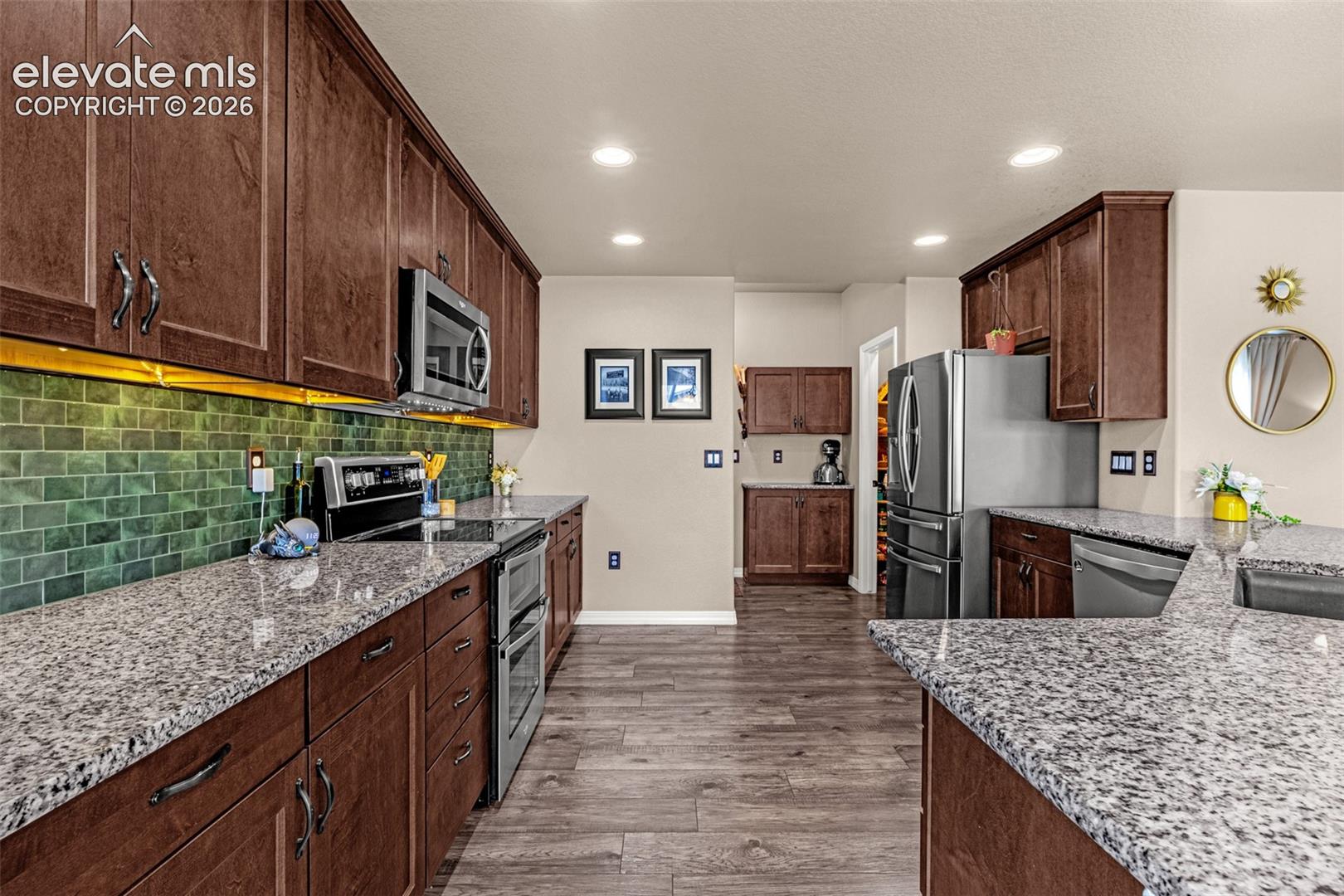 Kitchen with dark wood cabinets, granite counters, green tile backsplash, and stainless steel appliances.