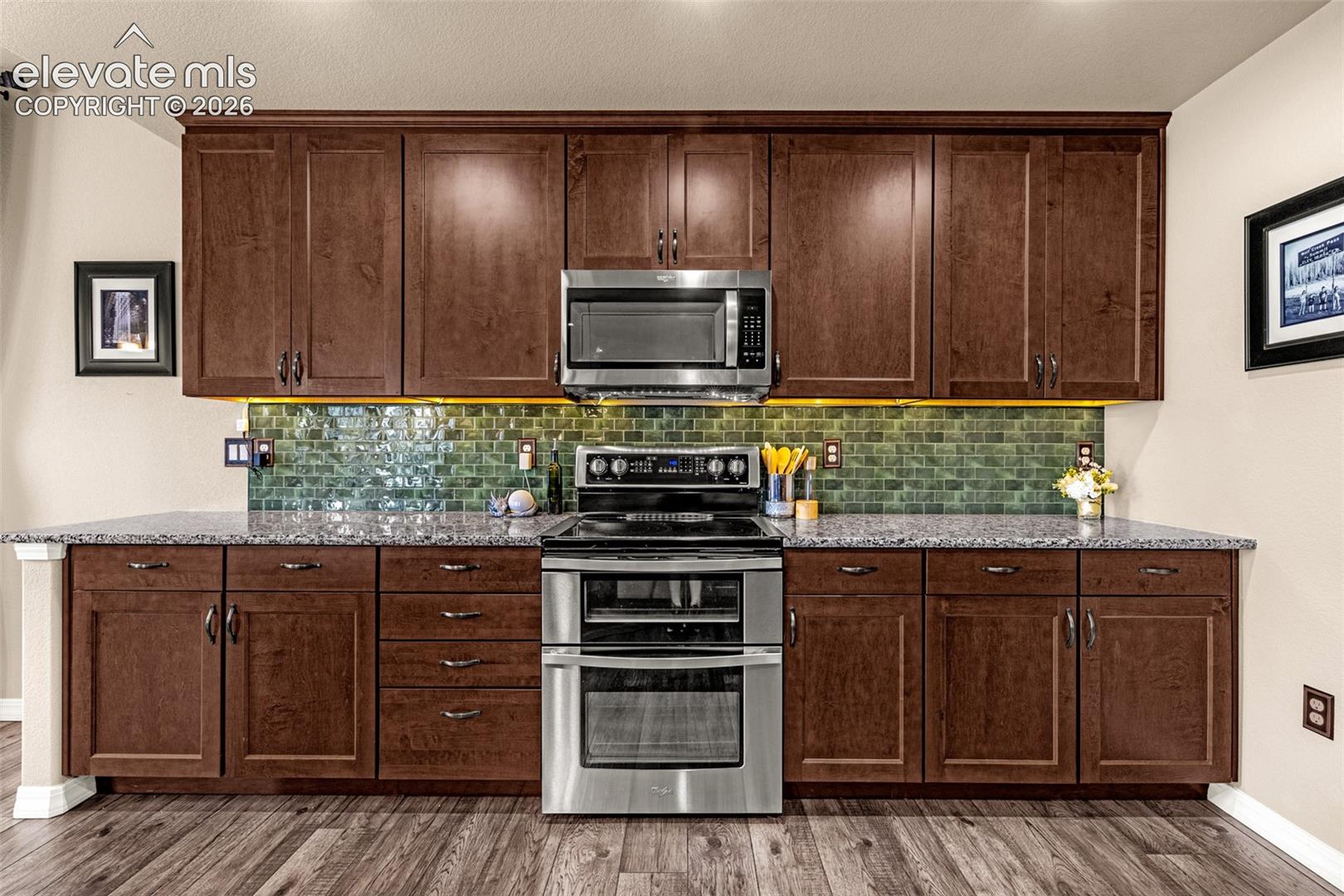 Kitchen with dark wood cabinets, green tile backsplash, granite counters, and stainless steel double oven.