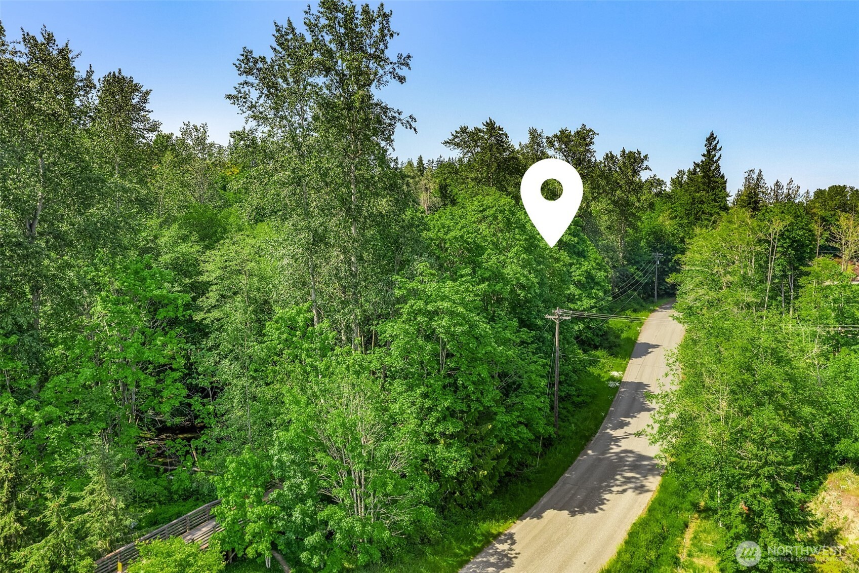 Aerial view of a wooded property beside a curving road, marked with a white location pin.
