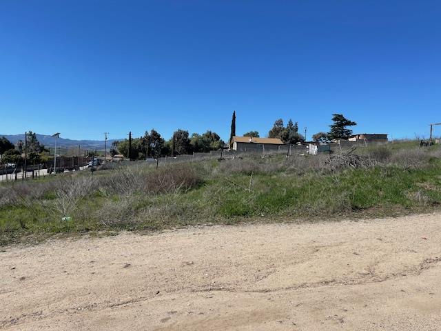 Vacant grassy lot beside a dirt road, with fencing and distant mountains.