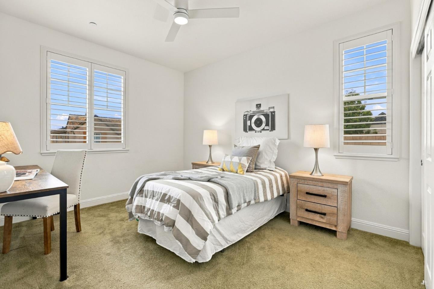 Staged bedroom with striped bedding, wooden nightstands, a desk, and shuttered windows.