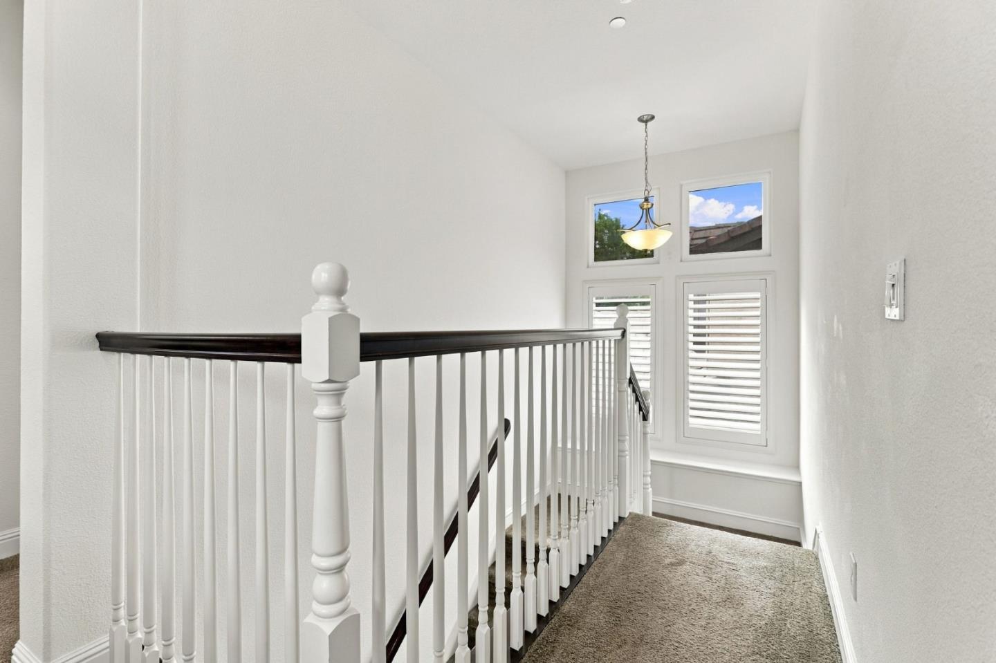 Upstairs landing with beige carpet, white stair railing, dark wood handrail, and shuttered windows.