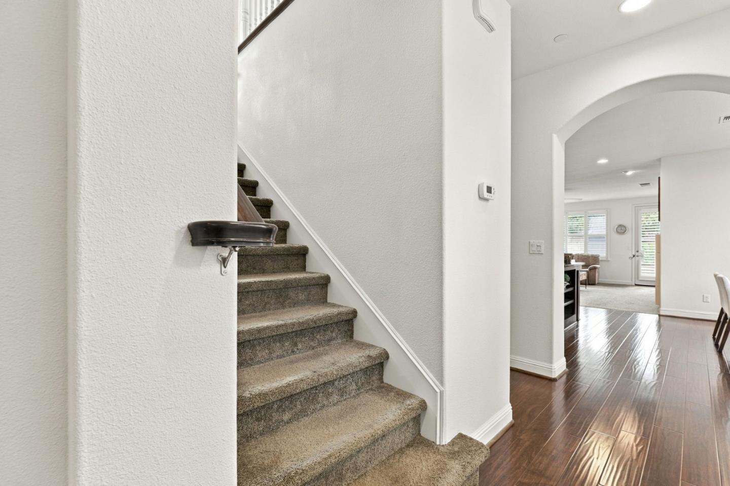 Carpeted staircase beside a wood-floored hallway leading through an arch to a bright living area.
