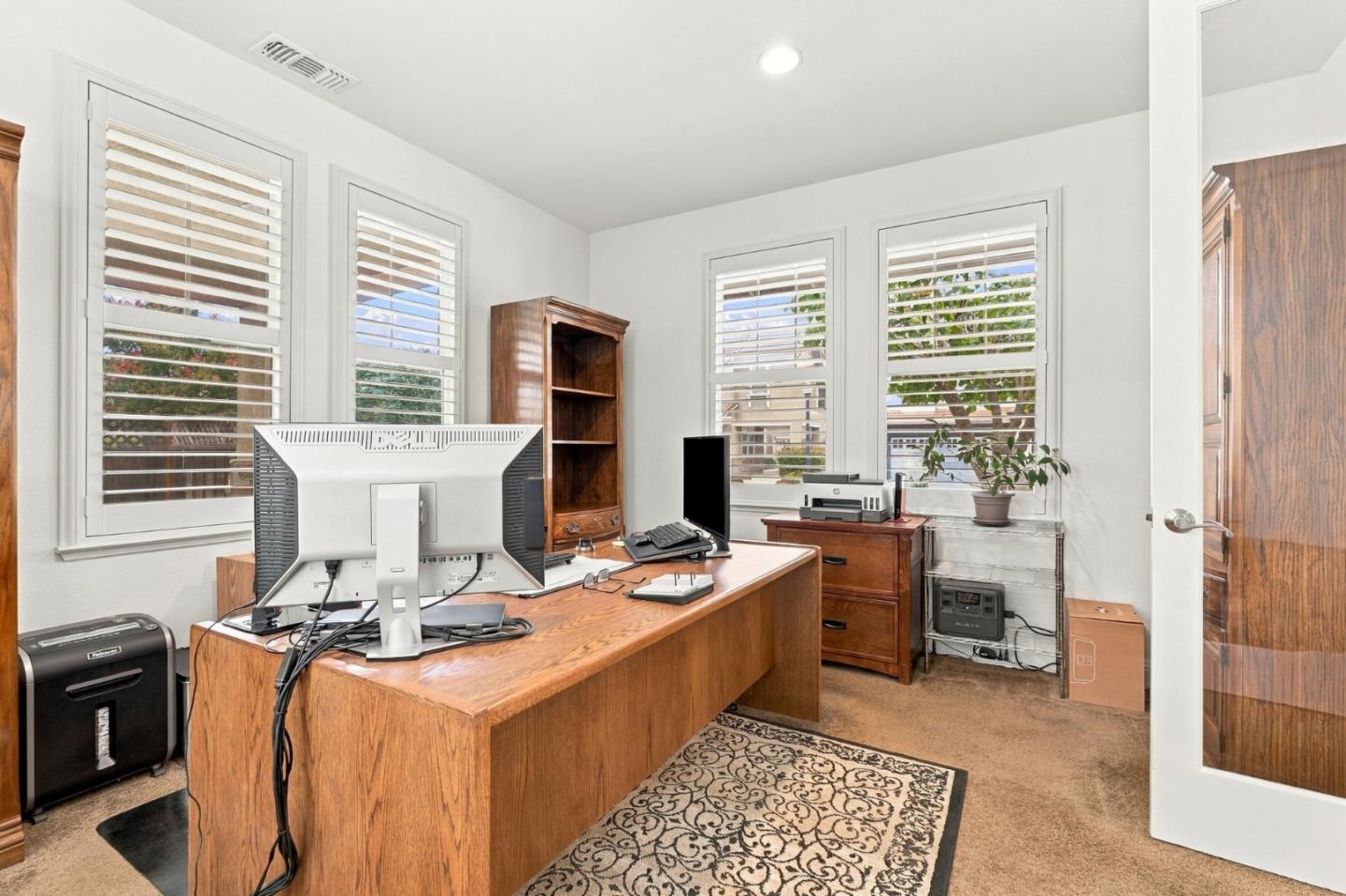 Home office with a large wooden desk, computer equipment, and tall shuttered windows.