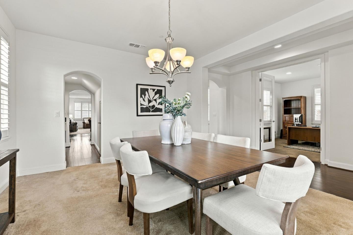 Dining room with a dark wood table, white chairs, and a chandelier, opening to adjoining rooms.