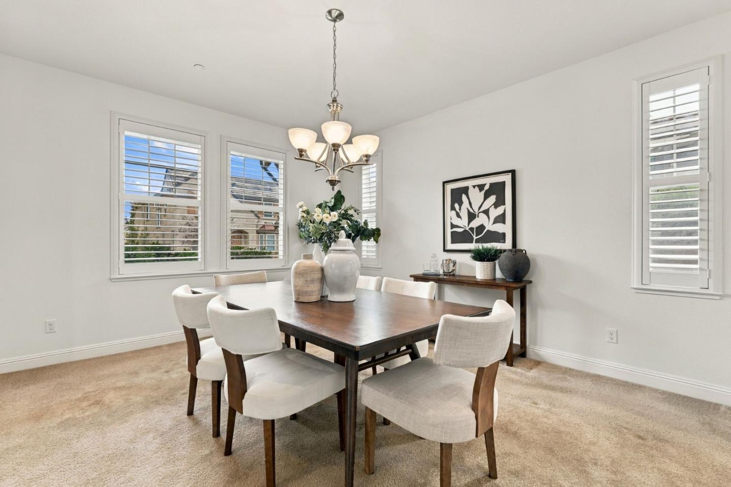 Dining room with a dark wood table, upholstered chairs, chandelier, and shuttered windows.