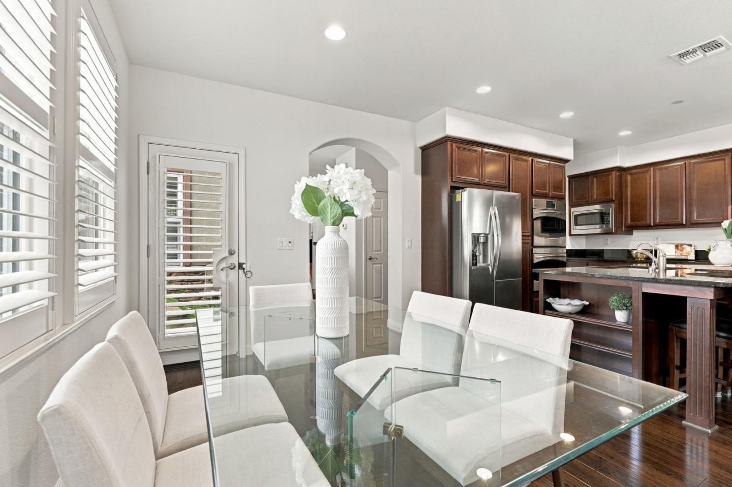 Dining area with a glass table and white chairs beside a kitchen with dark wood cabinets.