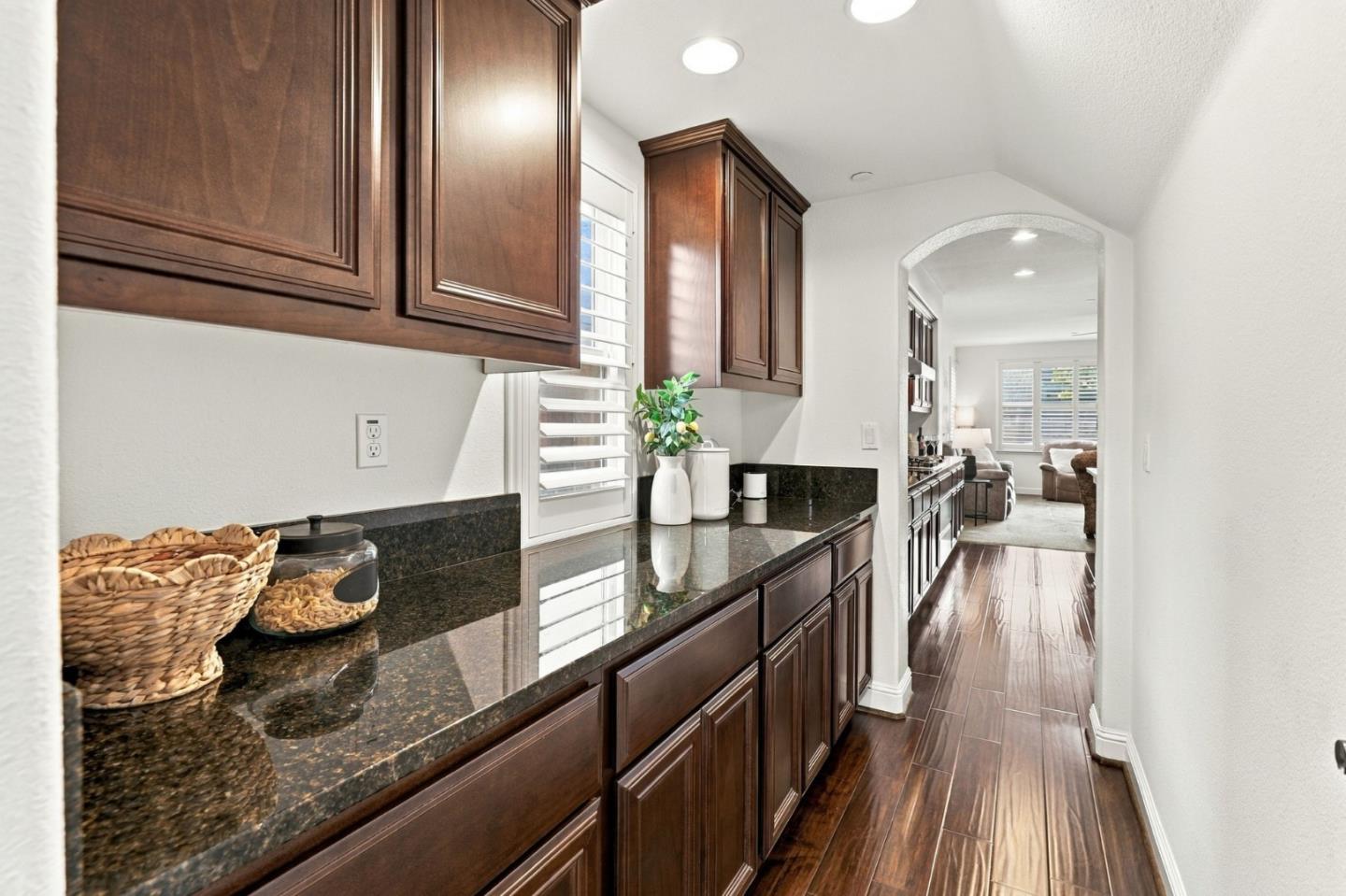 Kitchen passage with dark wood cabinets, granite counters, plantation shutters, and wood-look flooring.