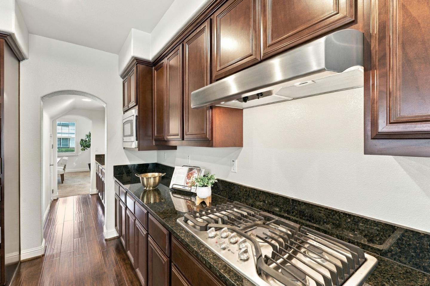 Kitchen with dark wood cabinets, granite counters, and a stainless steel gas cooktop beneath a wide hood.