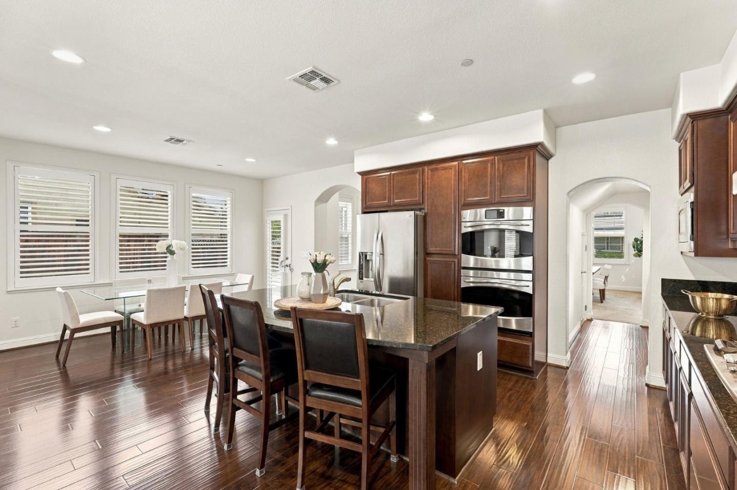 Kitchen with a granite island, dark wood cabinets, stainless steel appliances, and a glass dining table.