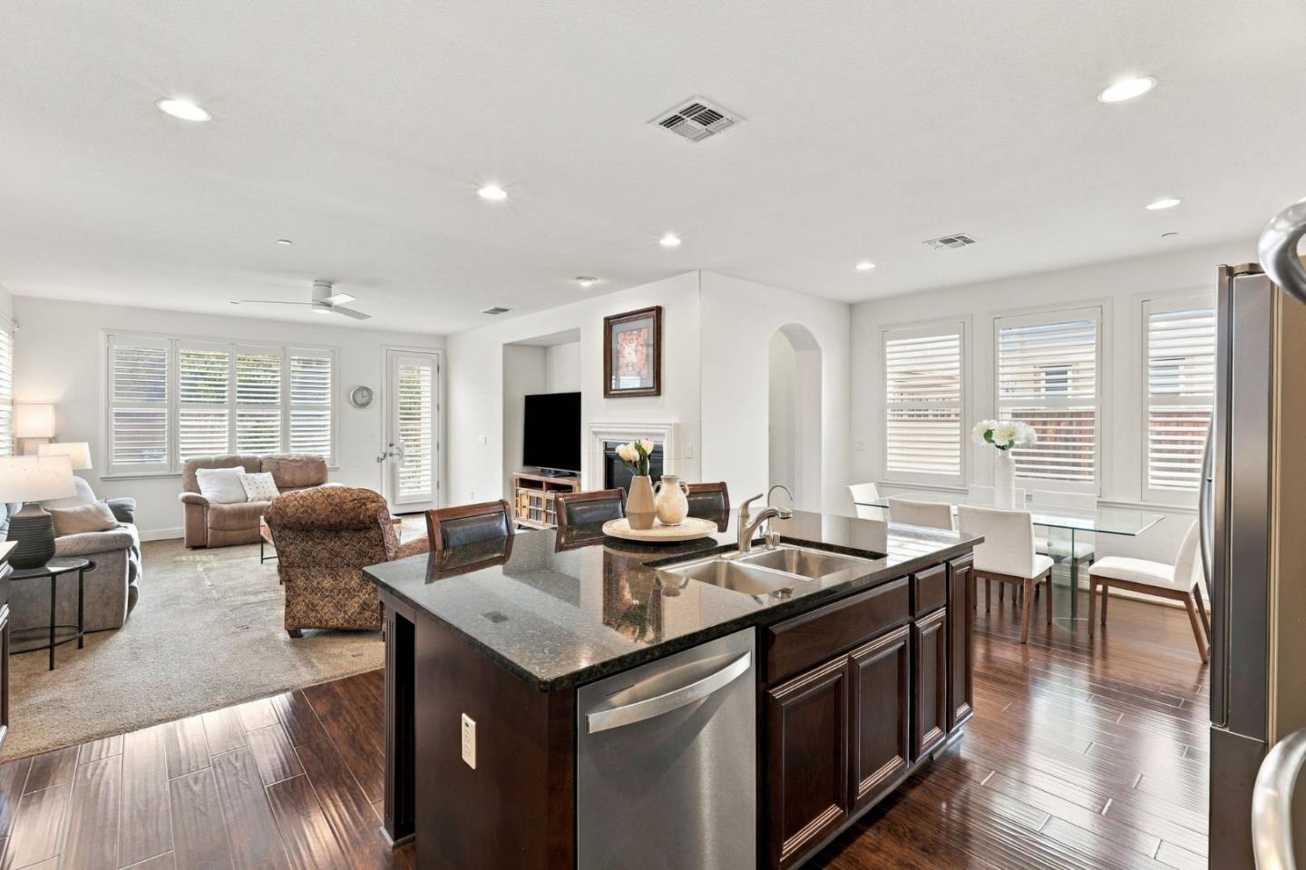 Open-plan kitchen and living area with a dark island, fireplace, and plantation shutters.