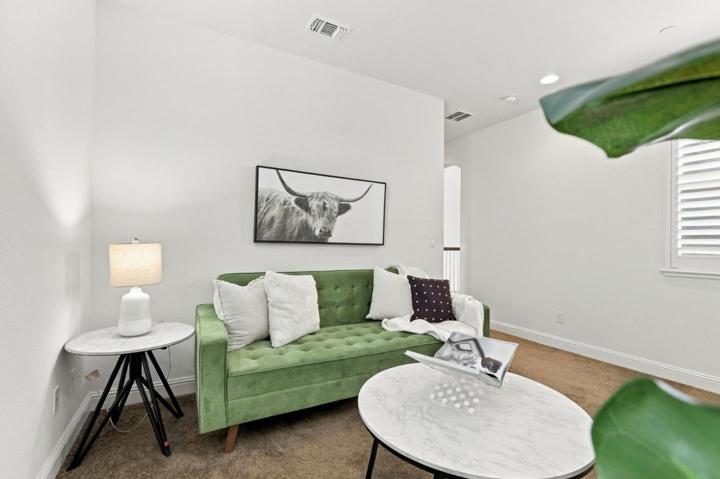 Living room with a green tufted sofa, marble-look tables, and a framed longhorn portrait.