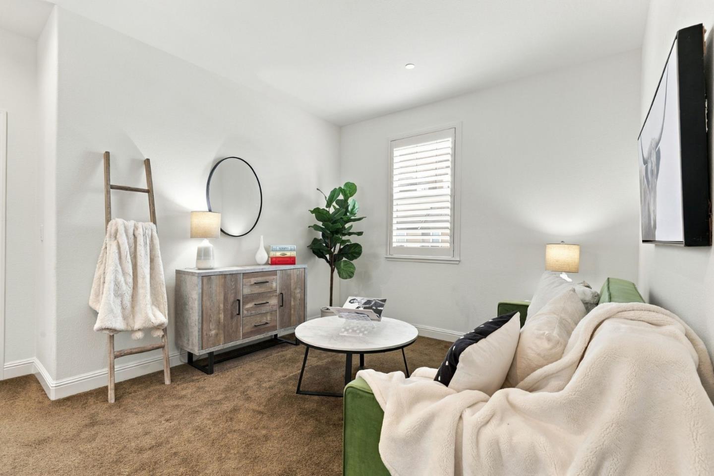 Staged living room with a green sofa, white throw, round coffee table, and shuttered window.
