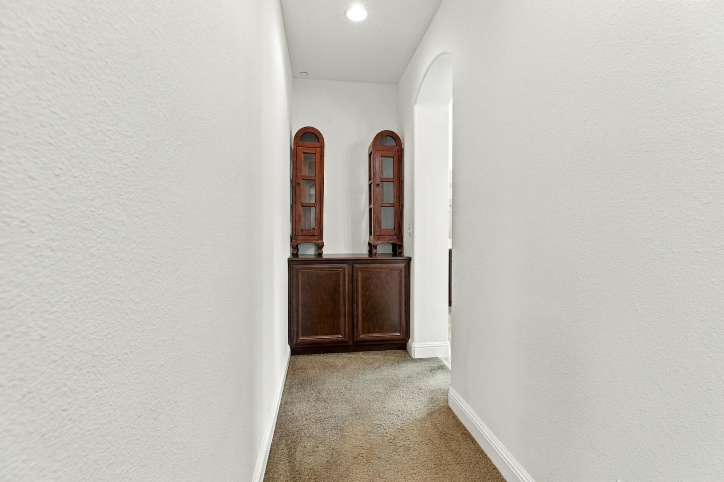 Carpeted hallway ending at a dark wood cabinet topped with two narrow display cabinets.