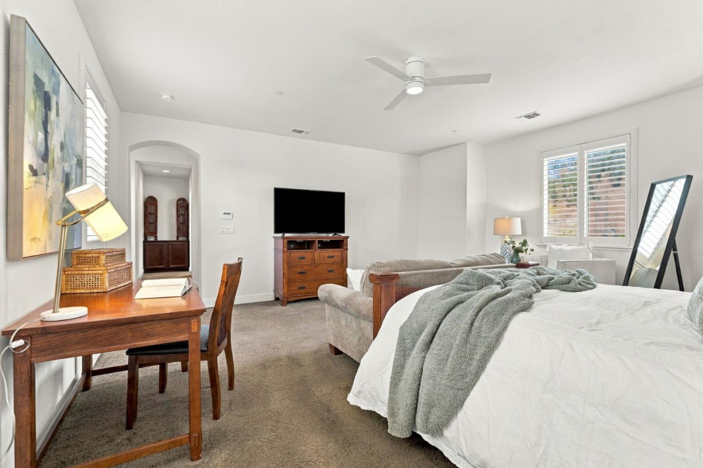 Bright bedroom with a large bed, wooden desk and dresser, and shuttered windows.