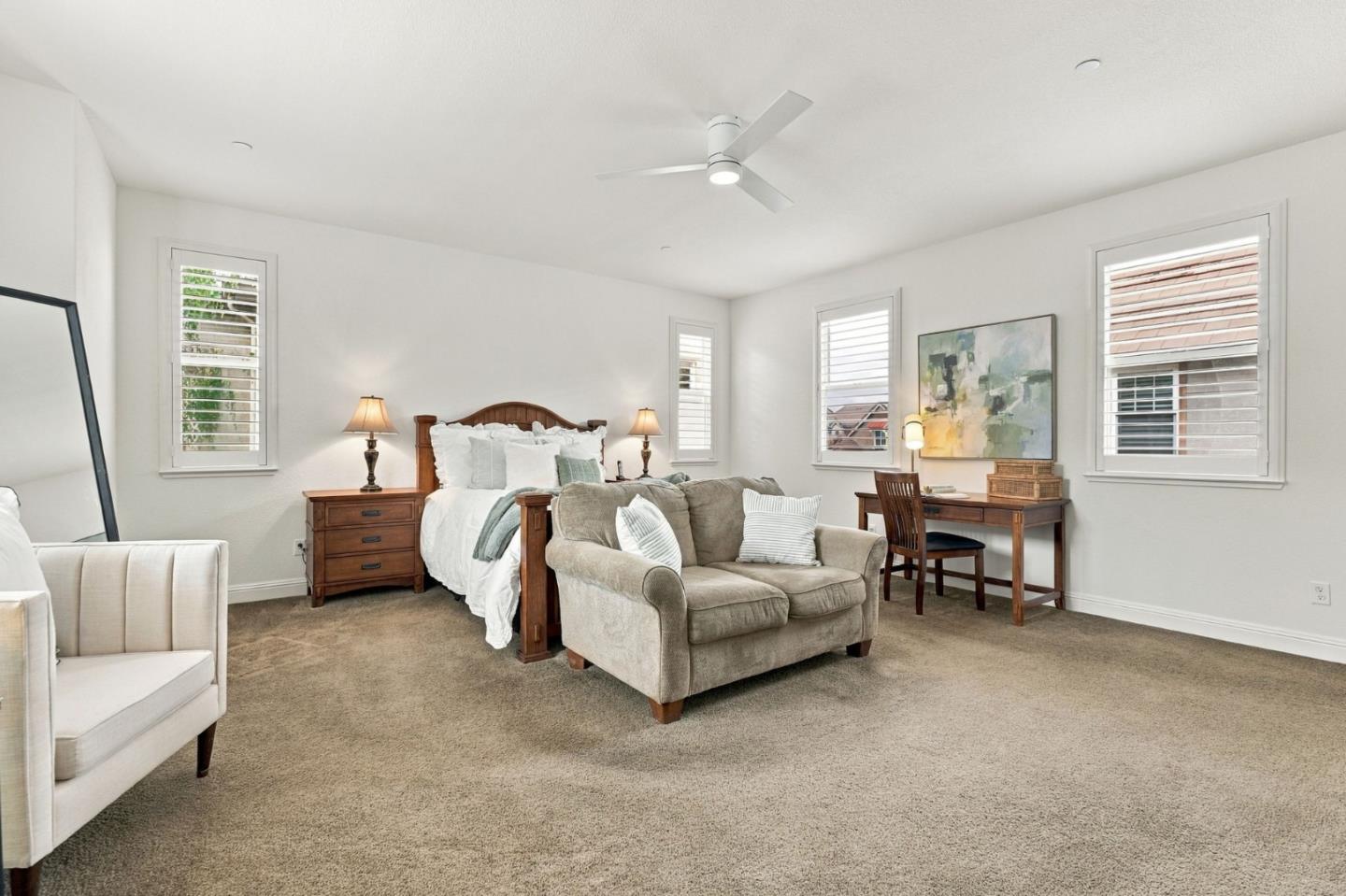 Bedroom with a wooden bed, beige loveseat, carpet, and shuttered windows.