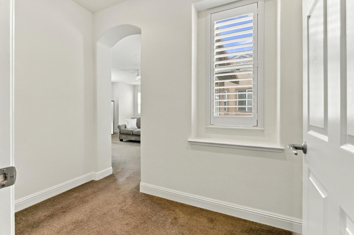 Carpeted hallway with an arched opening to a living room and a shuttered window.