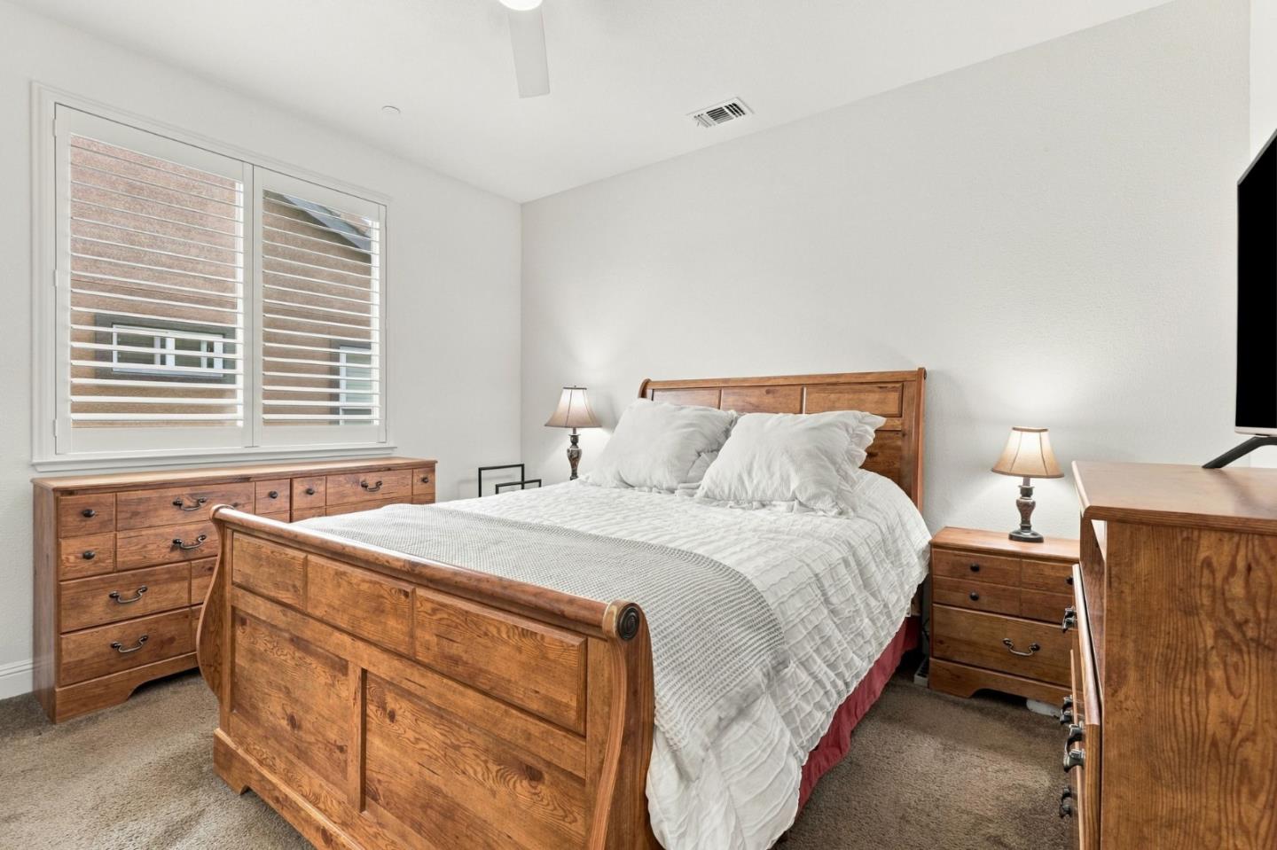 Bedroom with a wooden bed and matching dressers, white bedding, and a shuttered window.