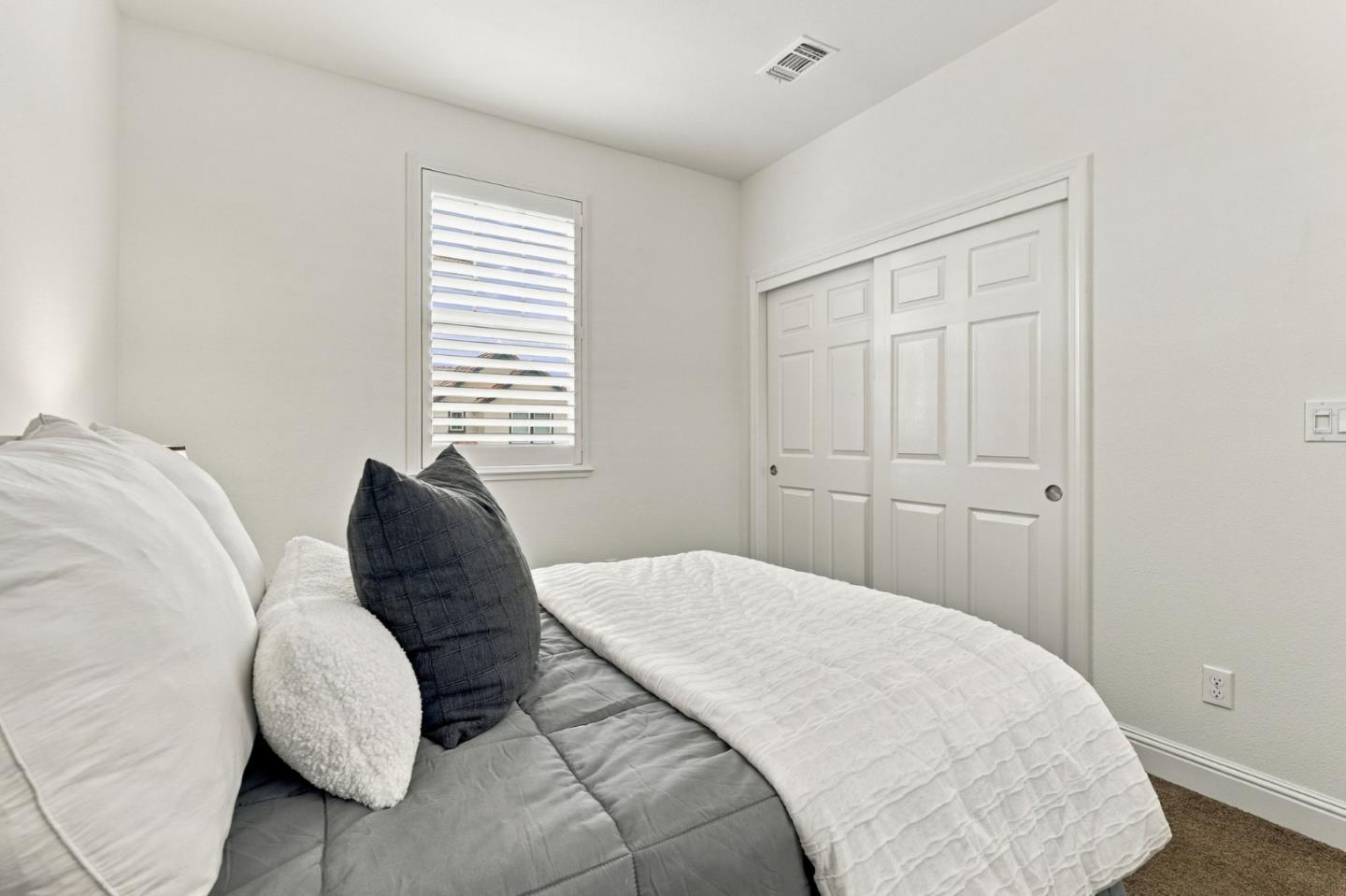 Bedroom with layered gray and white bedding, a shuttered window, and white sliding closet doors.