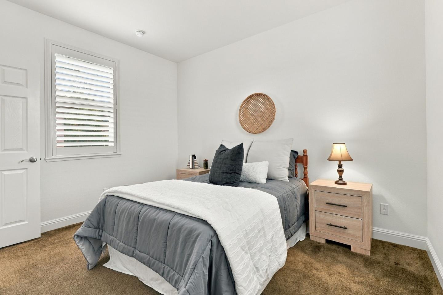 Bedroom with gray and white bedding, woven wall decor, and a shuttered window.