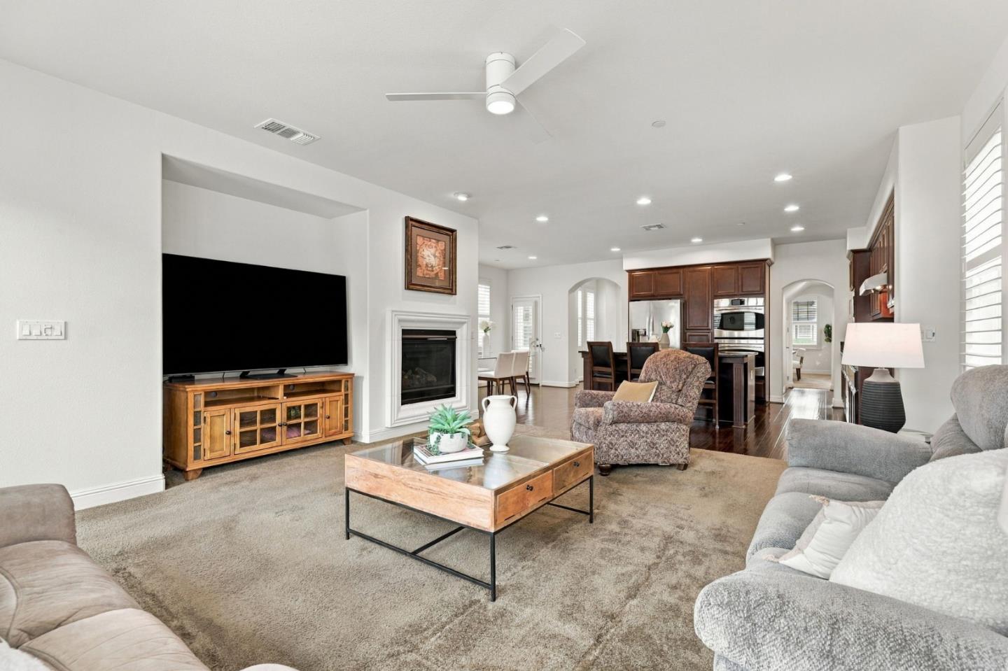 Living room with a fireplace and television, opening to a kitchen with dark wood cabinetry.