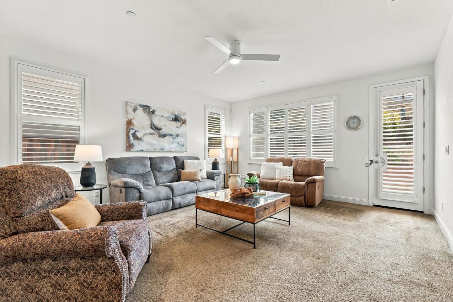 Furnished living room with plantation shutters, three sofas, and a wooden coffee table.