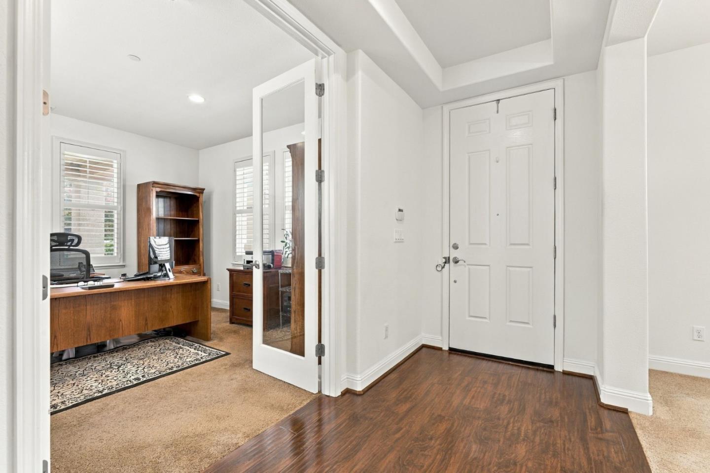 Entry foyer with dark wood flooring and a glass-paneled door opening to a furnished home office.