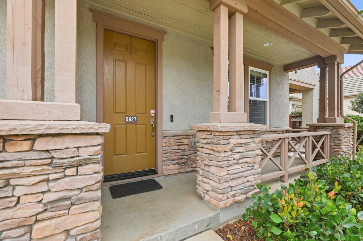 Covered front porch with a paneled wooden door, stone columns, and a wooden railing.