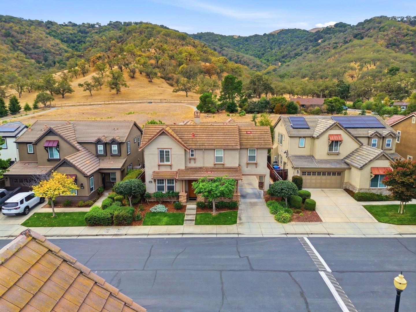 Two-story home with a tiled roof and landscaped yard, with rolling tree-covered hills behind it.