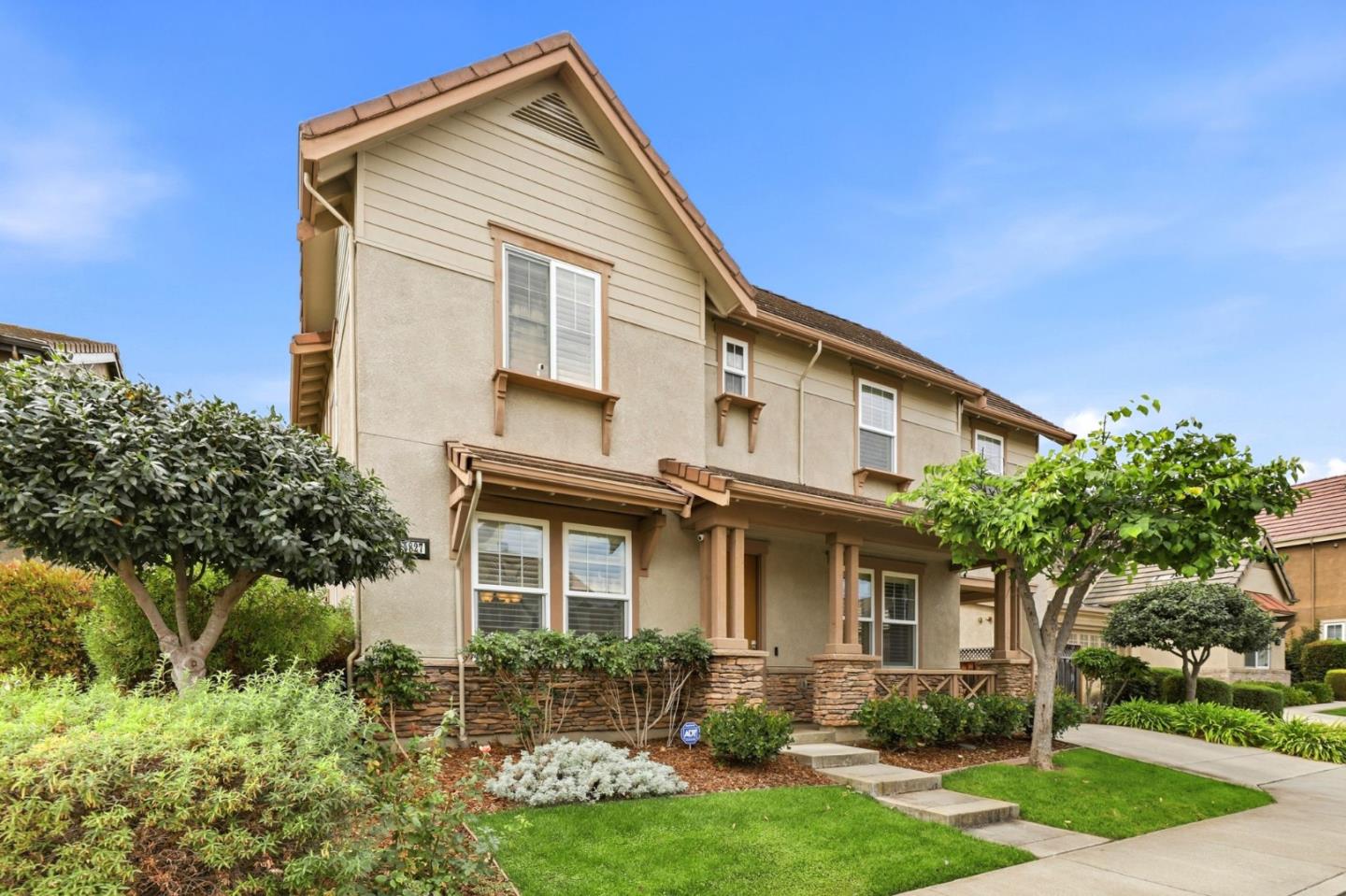 Two-story beige home with a covered porch, stone-accented facade, and landscaped front lawn.