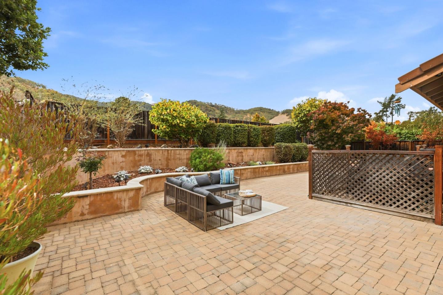 Backyard patio with a spacious paver terrace, outdoor sectional seating, landscaped beds, and hills beyond the fence.